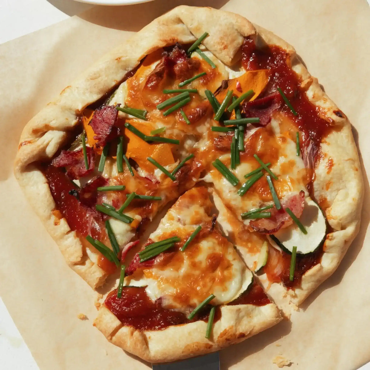 Homemade pizza with bacon, zucchini, cheese, and chives on parchment paper