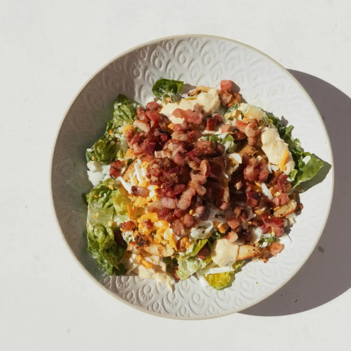 Crispy bacon & egg salad with fresh lettuce, cheese, and creamy dressing on a white plate