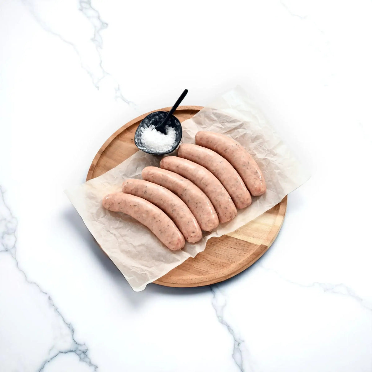 Raw pork truffle provolone sausages on parchment paper with salt bowl on wooden board
