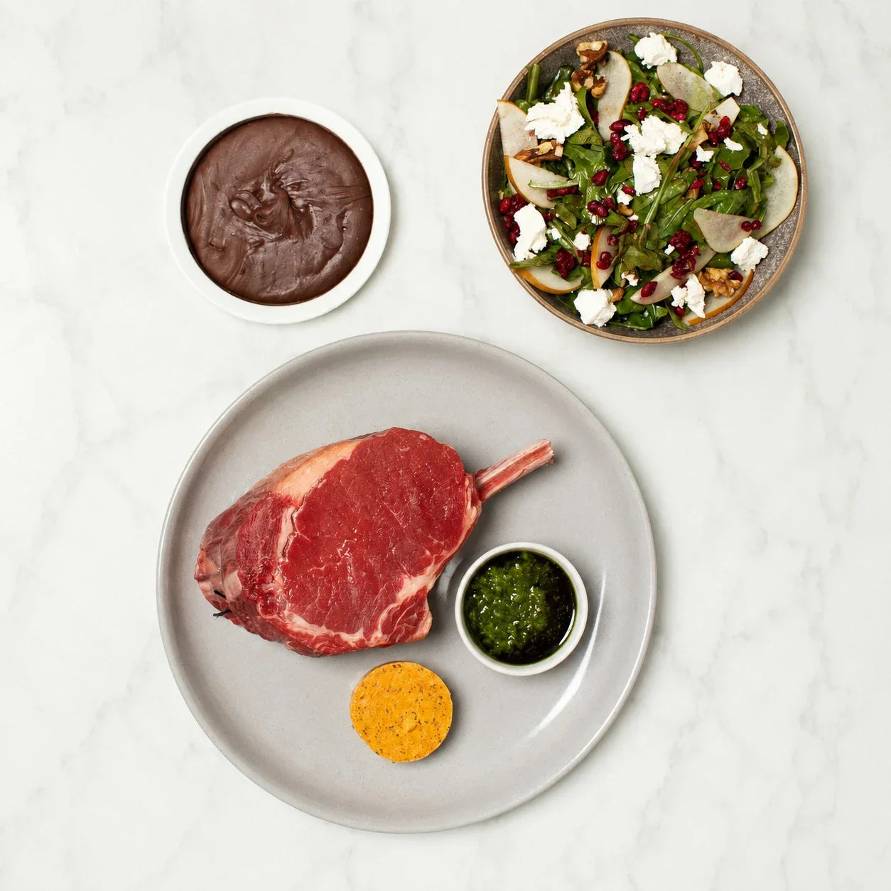 Raw Tomahawk steak with herb sauce, compound butter, chocolate dessert, and gourmet salad