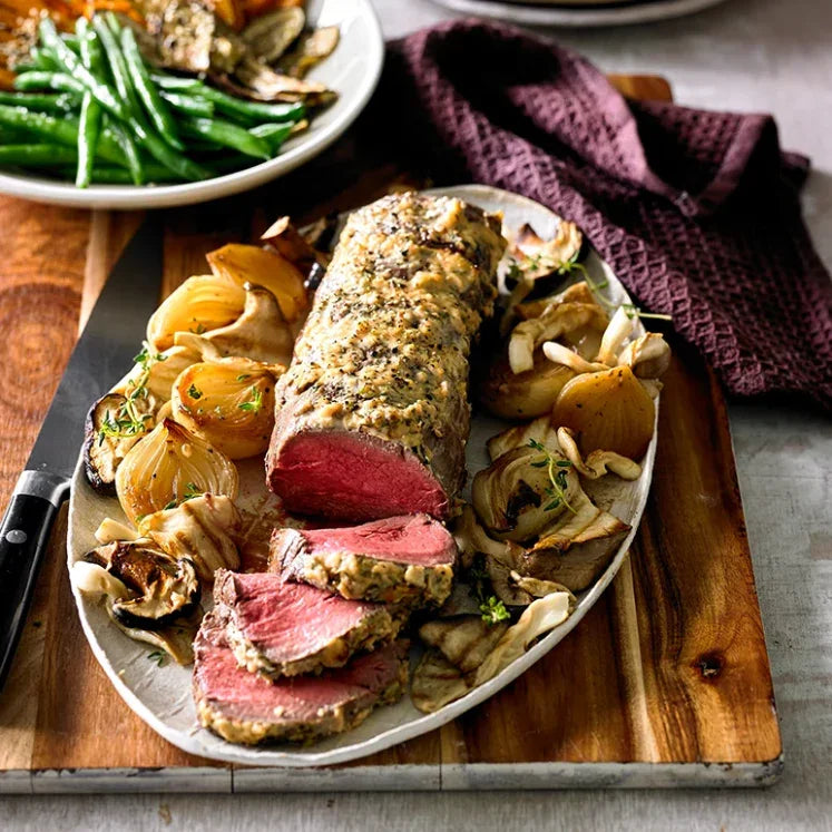Sliced Australian beef tenderloin roast with roasted onions and mushrooms on platter