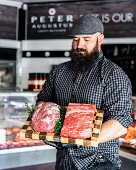 Bearded butcher at Peter Augustus holding premium Australian beef cuts on wooden board