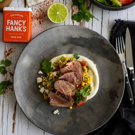 Sliced grilled beef with corn salsa and creamy sauce, garnished with cilantro and lime, featuring Fancy Hank's taco rub
