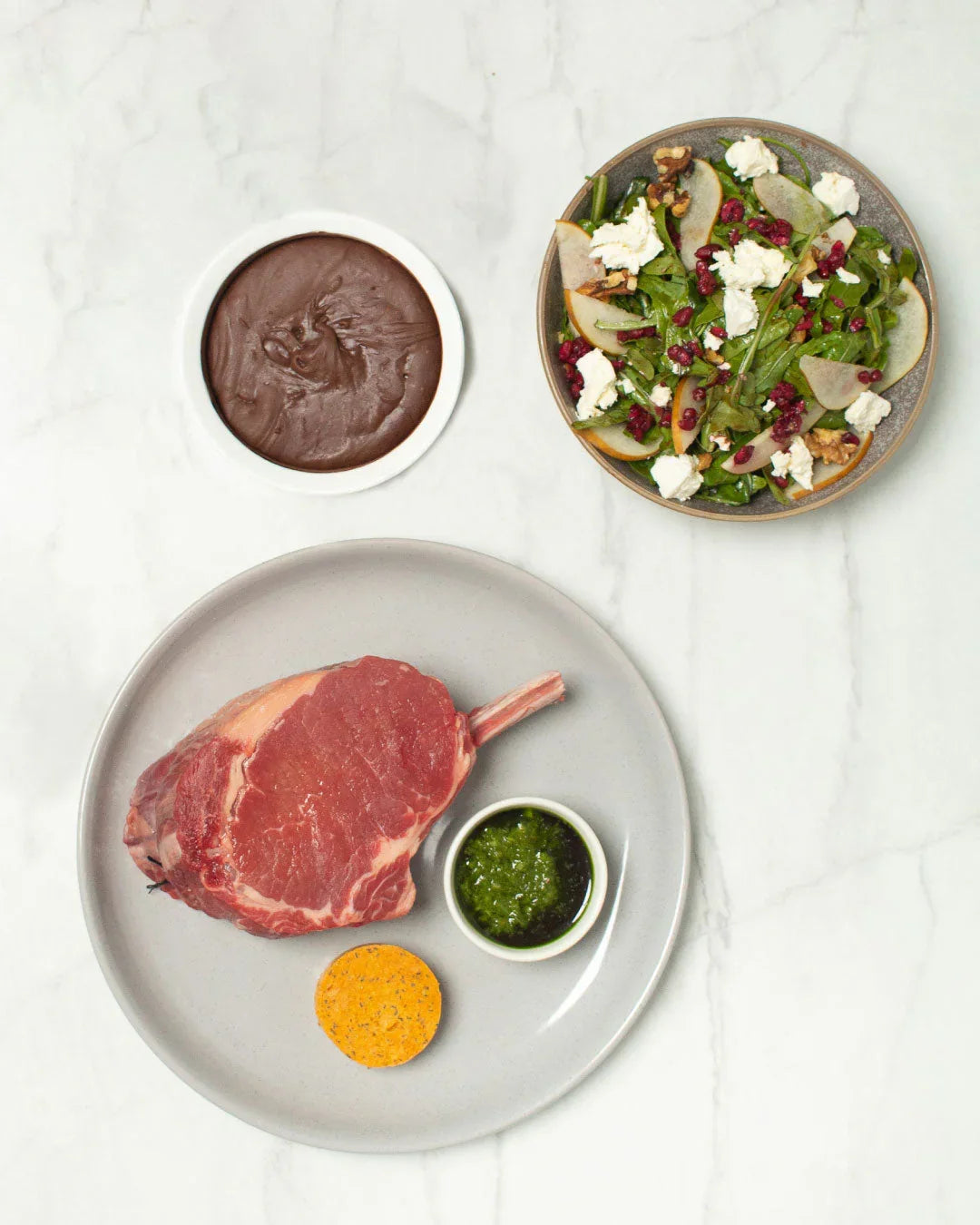 Raw Tomahawk steak with herb sauce, compound butter, chocolate dessert, and gourmet salad