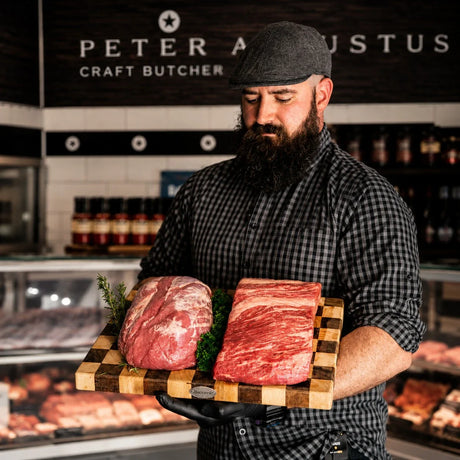 Bearded butcher at Peter Augustus holding premium Australian beef cuts on wooden board