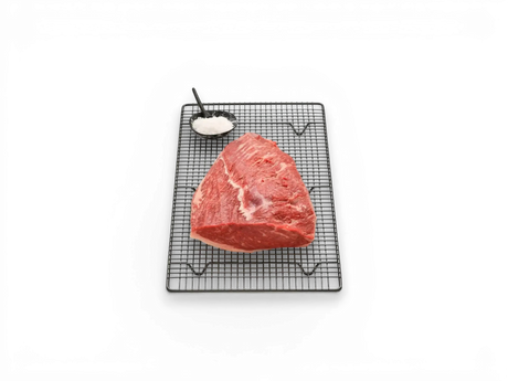 Raw Wagyu rump cap steak on wire rack with a bowl of coarse salt on marble background