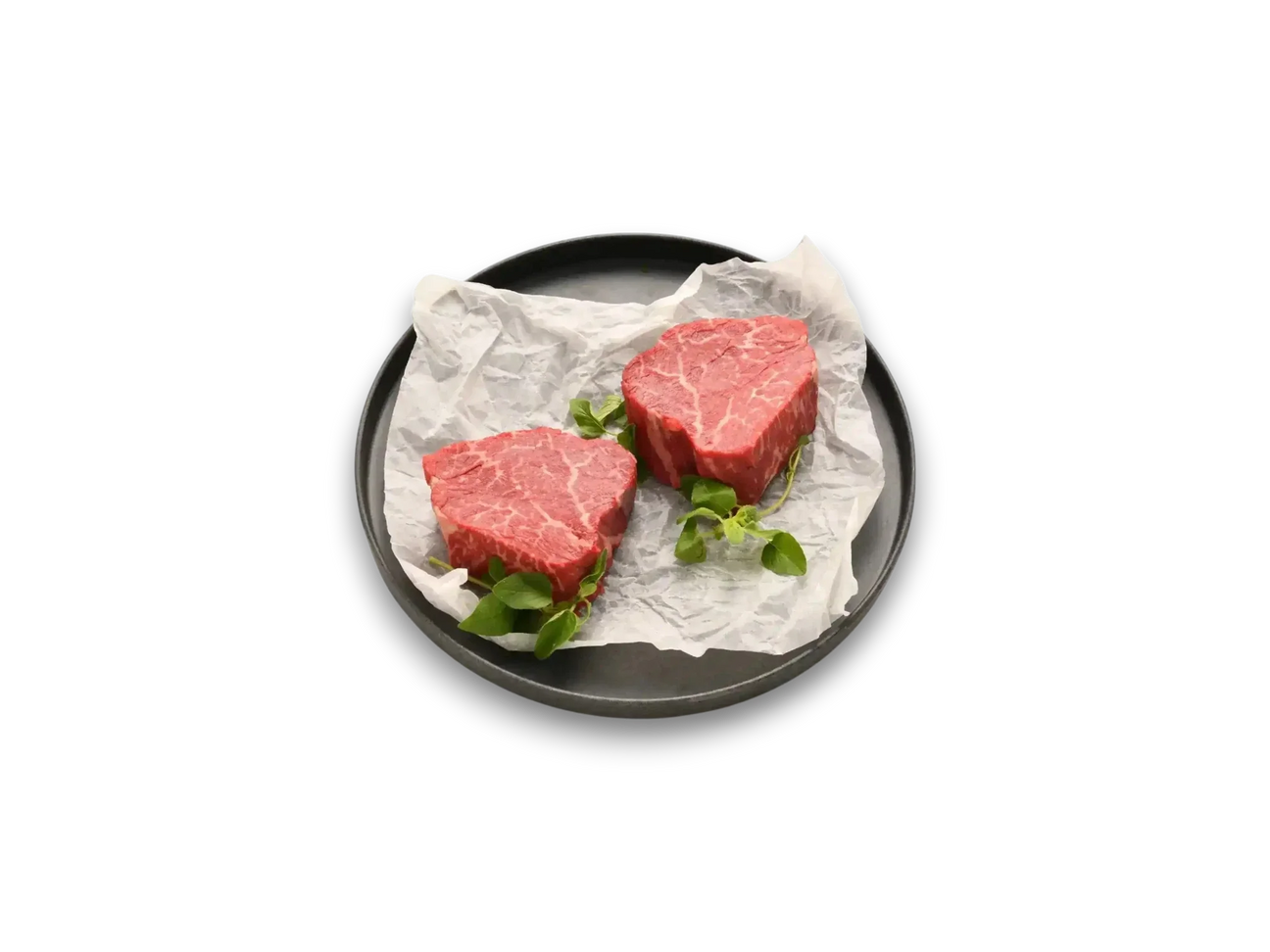 Two raw Wagyu eye fillet steaks with marbling on parchment paper, garnished with greens