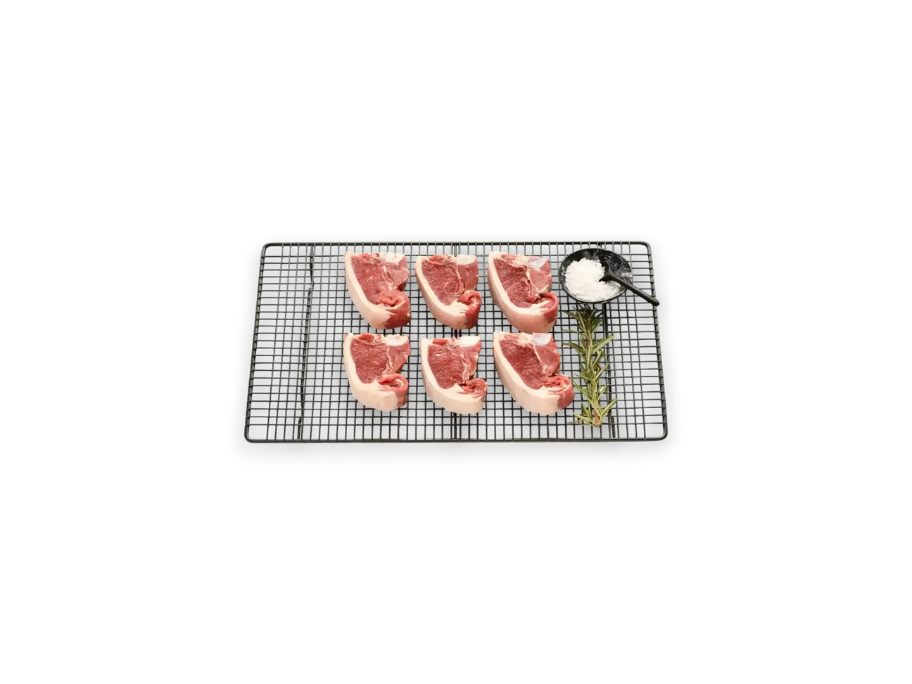 Six fresh lamb loin chops on a wire rack with rosemary and a small bowl of sea salt