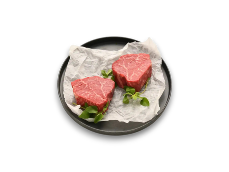 Two raw Wagyu eye fillet steaks with marbling on parchment paper, garnished with greens