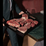 Assorted premium beef steaks with marbling on a serving tray in a restaurant setting.