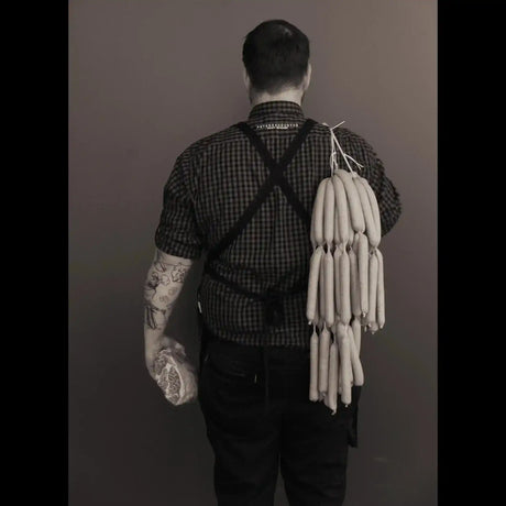 Tattooed butcher in checked shirt holding premium sausages and marbled beef, Peter Augustus