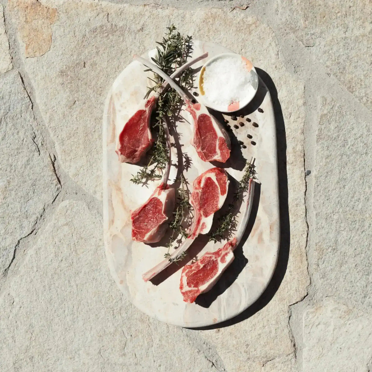 Raw lamb cutlets with herbs and salt on a stone platter, gourmet meat presentation