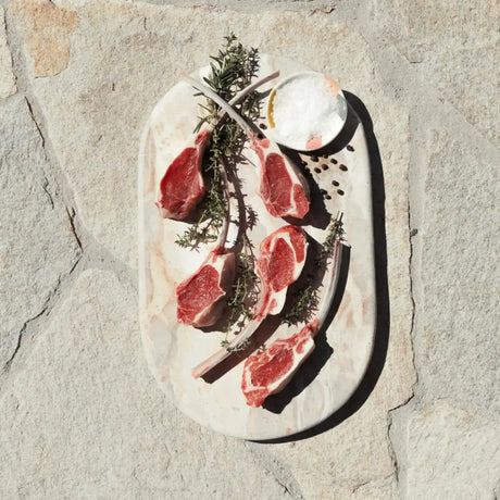 Raw lamb cutlets with herbs and salt on a stone platter, gourmet meat presentation