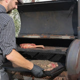 Butcher placing seasoned premium beef cuts, including tomahawk steak, in a smoker grill outdoors