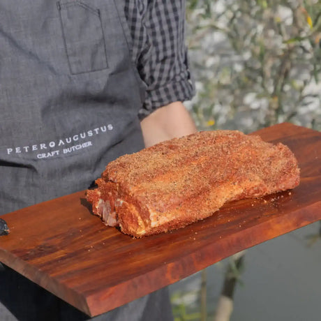 Seasoned beef roast on a wooden board, held by butcher in apron outdoors