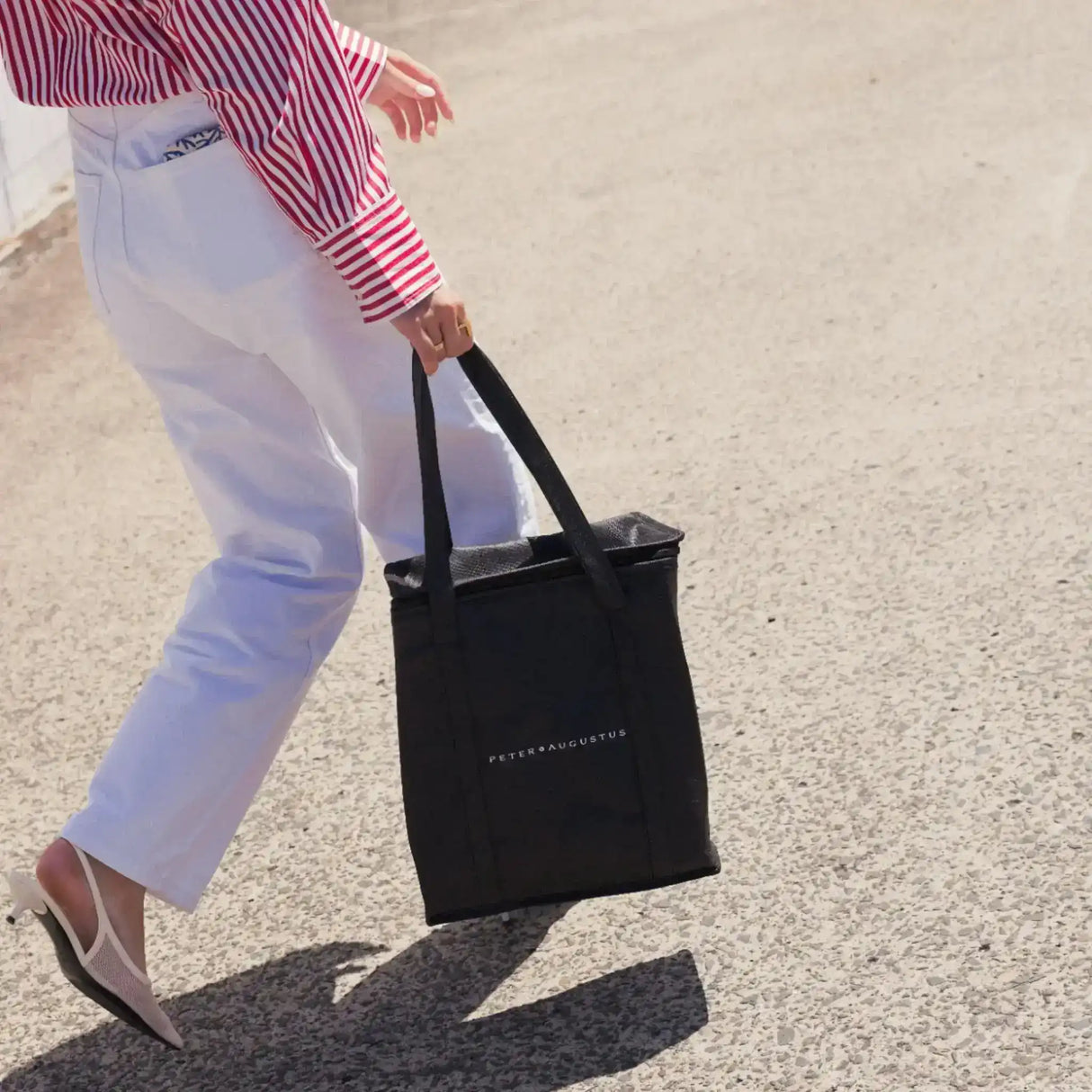 Person carrying a Peter Augustus branded black tote bag outdoors