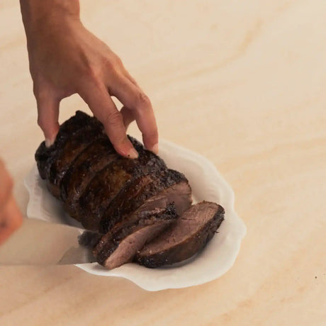 Hand slicing premium Australian beef roast on a white plate from Peter Augustus Craft Butcher