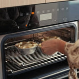Person placing homemade pies in round foil trays into a modern oven for baking.
