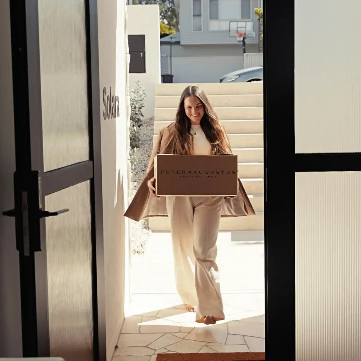 Woman smiling while delivering a Peter Augustus Craft Butcher box to a doorstep