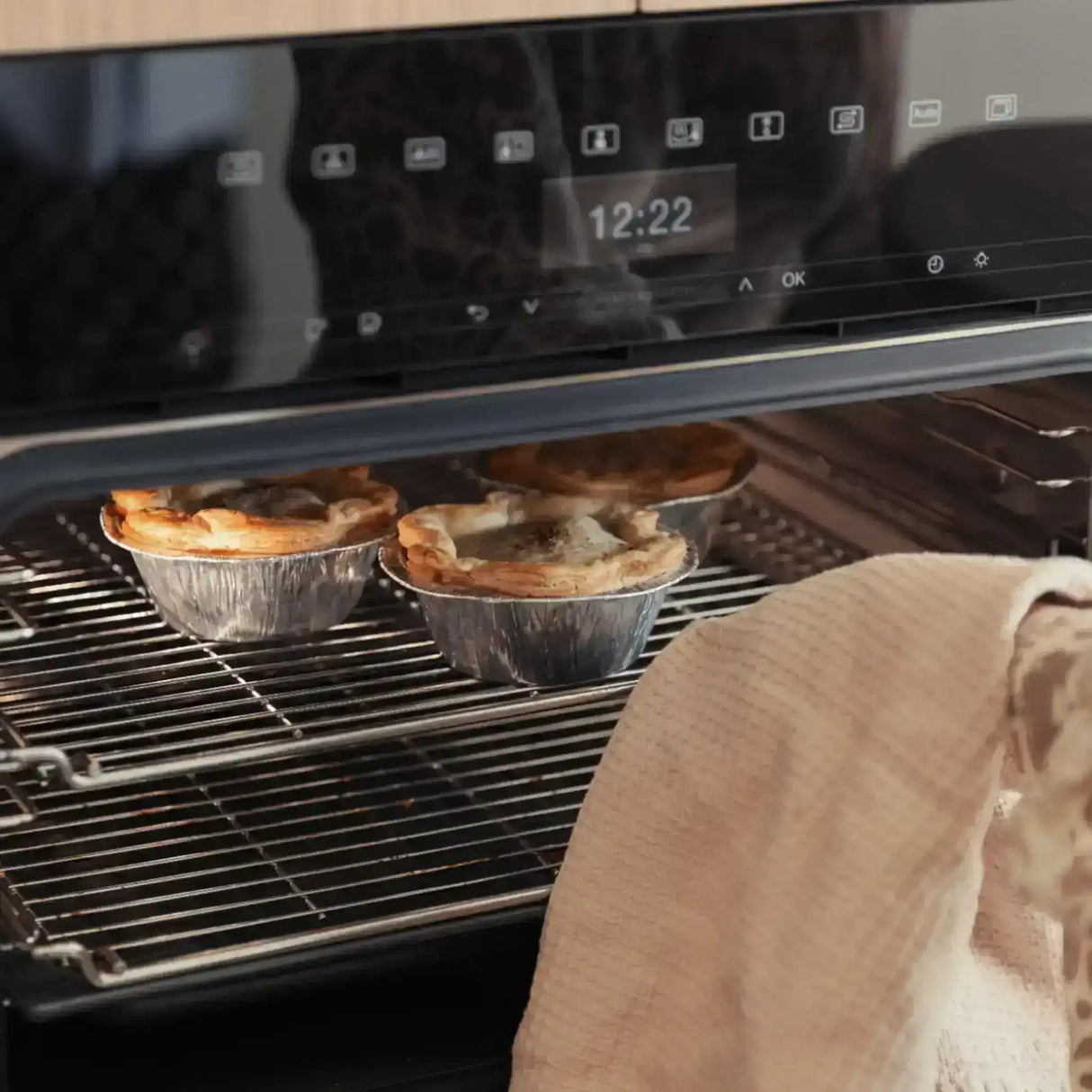 Freshly baked meat pies in foil trays on an oven rack, ready to serve.