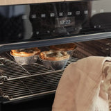 Freshly baked meat pies in foil trays on an oven rack, ready to serve.