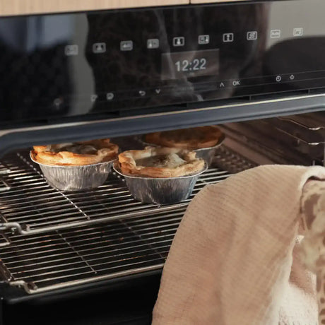 Three golden beef pies in foil trays baking in an oven, by Peter Augustus Craft Butcher.