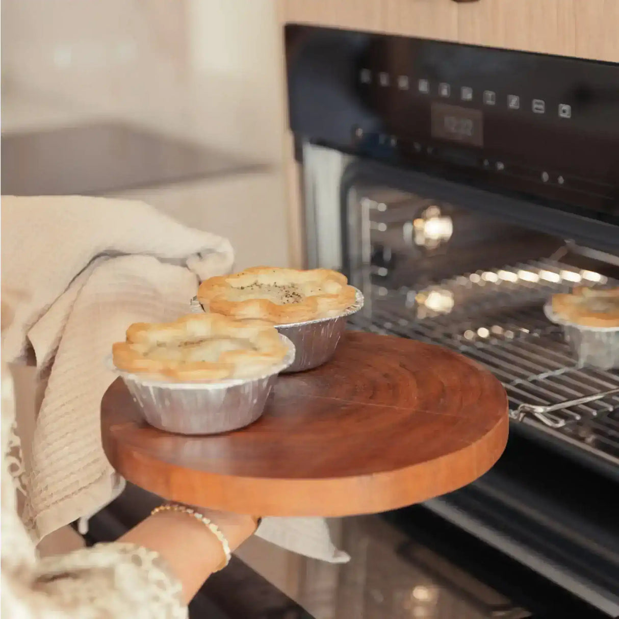 Freshly baked savory pies in foil tins being removed from the oven on a wooden board