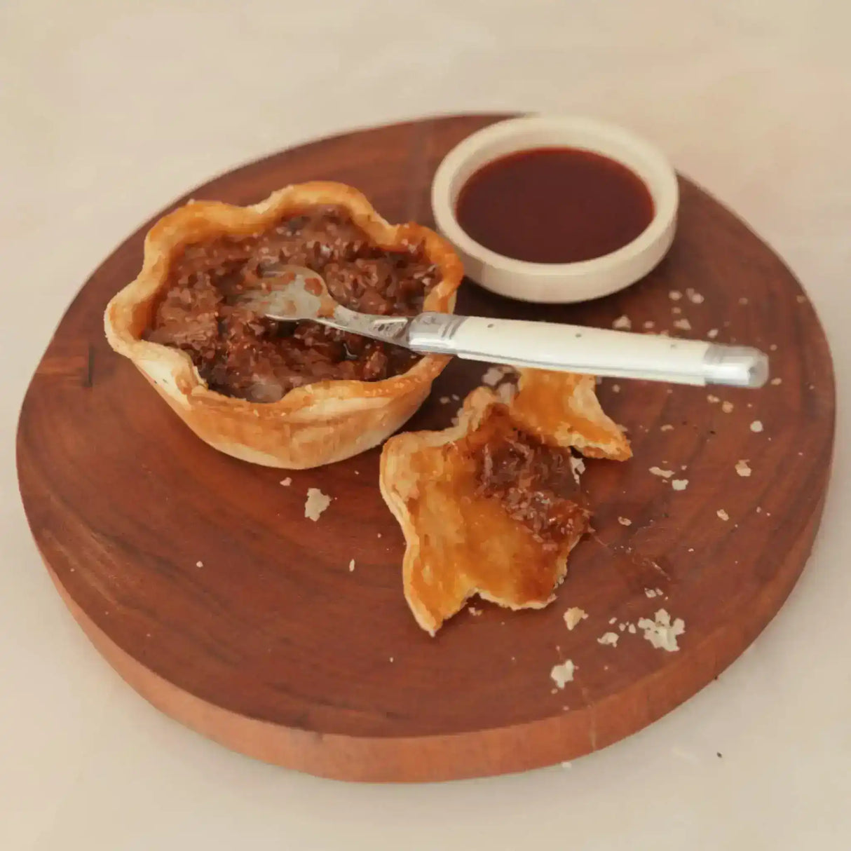 Australian beef meat pie with flaky pastry, brown sauce, and knife on wooden board