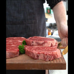Craft butcher presenting premium marbled Australian beef steaks on a wooden board