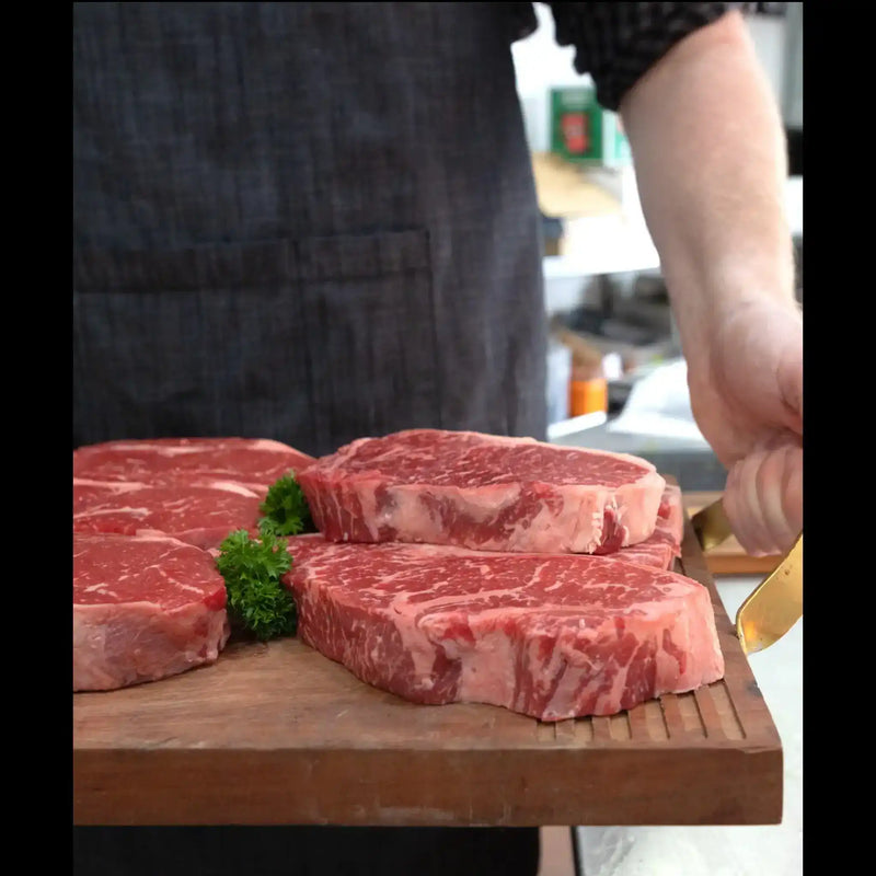 Craft butcher presenting premium marbled Australian beef steaks on a wooden board