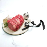 Raw Wagyu rump roast on marble board with garlic, rosemary, ribbon, and Christmas ornaments