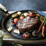 Grilled beef steak with roasted baby potatoes, cherry tomatoes, carrots, and garlic on a black plate
