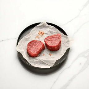 Raw Angus eye fillet steaks on parchment with sea salt on a black plate, marble background