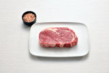 Raw Angus rib fillet steak on white plate with bowl of pink Himalayan salt