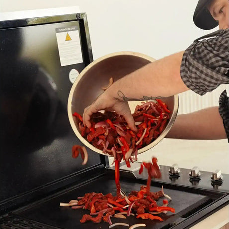 Person grilling premium Australian beef strips with red peppers and onions on a barbecue