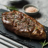 Cooked Angus beef steak garnished with herbs and salt on black slate with rosemary sprigs