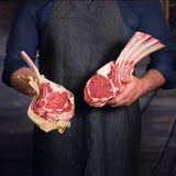 Butcher holding two raw grain fed tomahawk steaks with bone, marbled beef on display