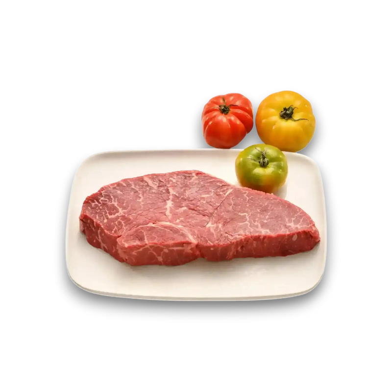 Freshly butchered marbled beef steak on white plate with heirloom tomatoes, showcasing premium grass-fed quality