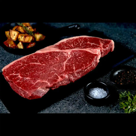 Raw Australian Black Onyx rump steak on a black slate with salt, pepper, and roasted potatoe