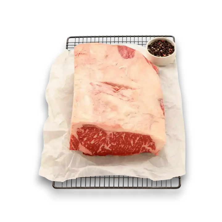 Premium Black Onyx Angus Sirloin roast with marbling, on parchment over rack, beside peppercorns