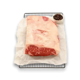 Premium Wagyu beef roast with marbling, on parchment over rack, beside peppercorns