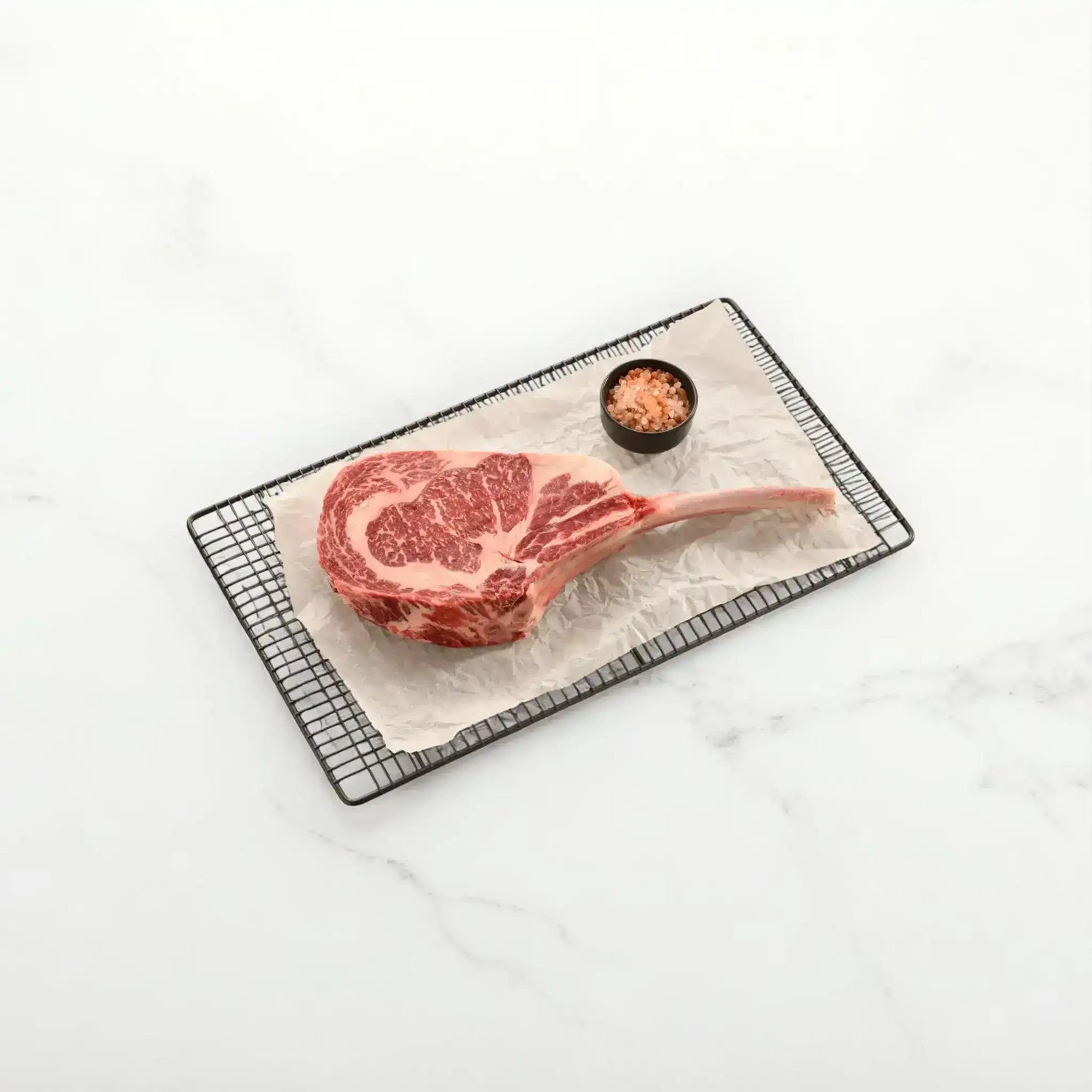 Raw Black Onyx Tomahawk_SB 5 steak on a cooling rack with a small bowl of salt