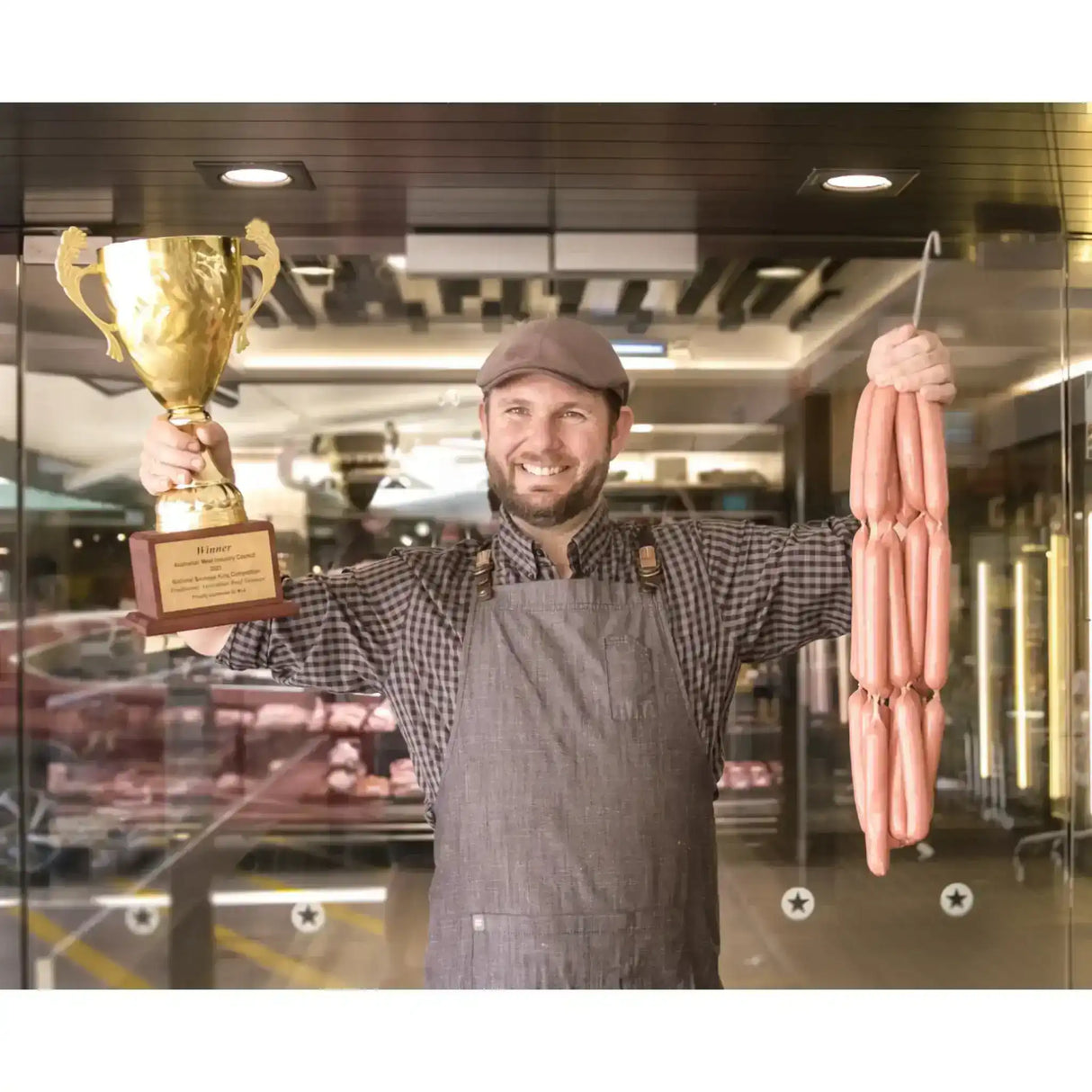 Smiling butcher holding a trophy and a string of gourmet sausages in a butcher shop