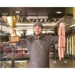 Award-winning butcher at Peter Augustus holding trophy and gourmet sausages, smiling in shop