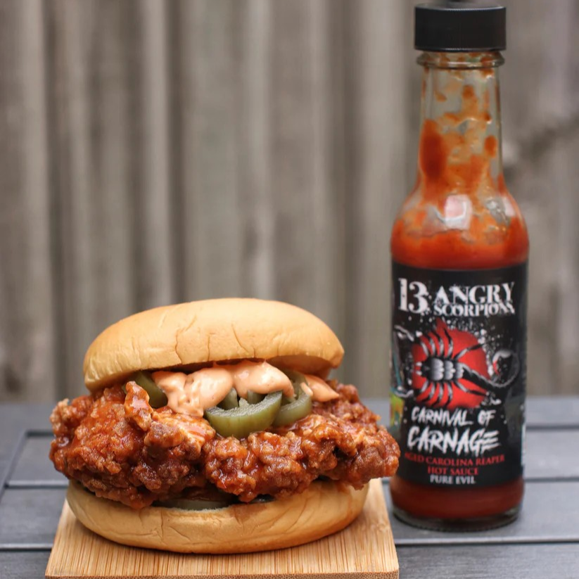 Burger with spicy chicken and jalapeños next to a bottle of 13 Angry Scorpions  Delicious hot sauce