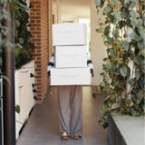 Person carrying three Peter Augustus Craft Butcher delivery boxes in a bright hallway with plants