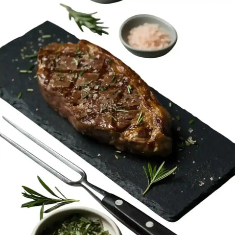 Diamantina Angus sirloin steak on slate with rosemary, salt, pepper, and carving fork