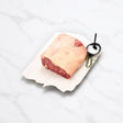 Raw Angus striploin half cut on parchment with salt and herbs on white marble surface