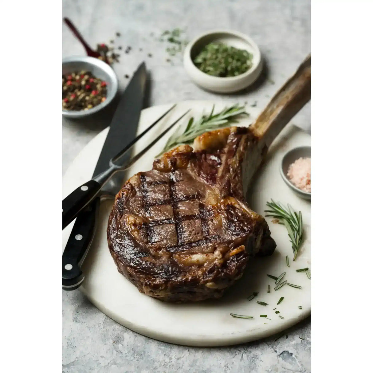 Grilled Angus tomahawk steak on marble board with rosemary, salt, and pepper bowls