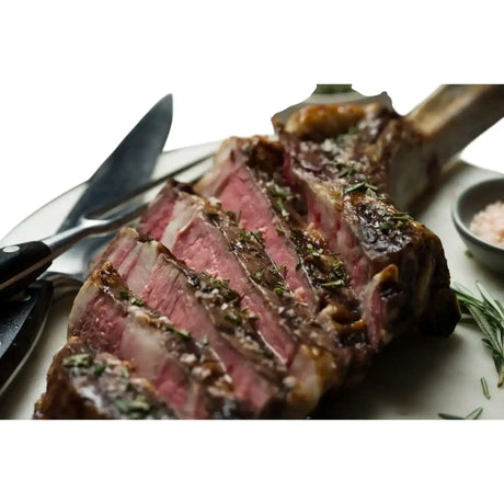 Sliced Diamantina Angus Tomahawk steak with herbs, gourmet salt, and cutlery on a plate, premium Australian beef from Peter Augustus